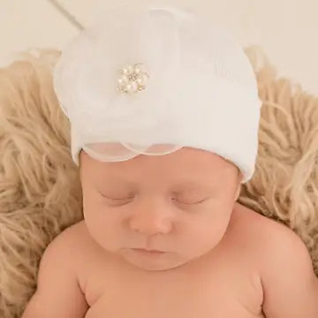 Newborn baby wearing white hospital hat with silk flower and pearl embellishment