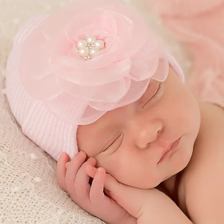 Newborn baby girl wearing pink and white striped hospital hat with layered chiffon flower and rhinestone cente