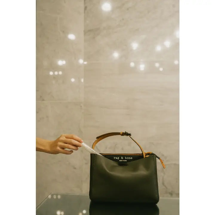 Hand holding purse-size anti-static spray next to green leather handbag - portable static cling solution lifestyle photography