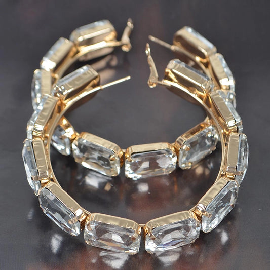 Gold-plated emerald-cut cubic zirconia XL hoop earrings shown on dark background, displaying continuous stone setting and brilliant sparkle
