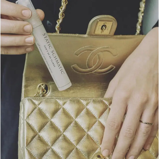 Woman using purse-size anti-static spray from gold quilted designer handbag - compact travel size static eliminator lifestyle photography