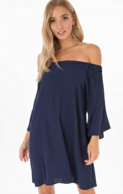 A woman modeling an off-the-shoulder navy blue shift dress with three-quarter bell sleeves against a plain white background.