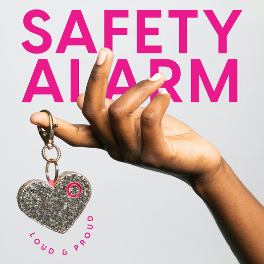 Hand holding a rose gold heart-shaped keychain with 'Safety Alarm' text above on a light gray background
