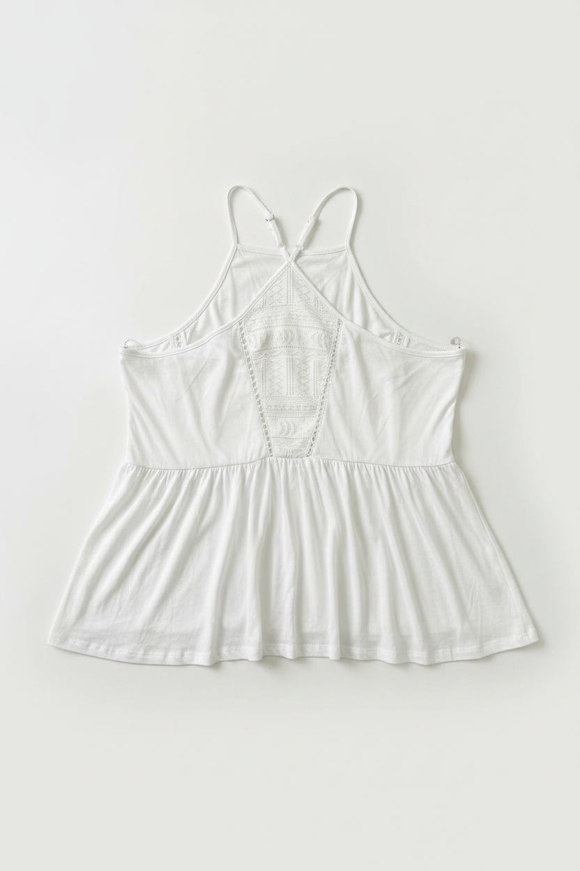 A white camisole-style top with thin straps, a gathered peplum waist, and lace-up back details, laid flat against a light off-white background.