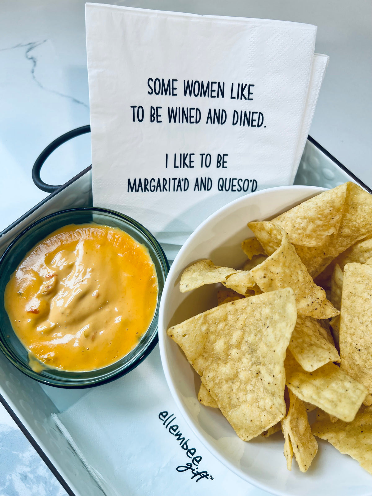 Funny margarita and queso cocktail napkins displayed with tortilla chips and cheese dip on marble surfacecount