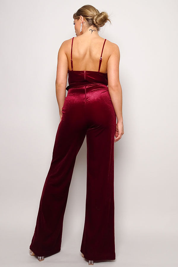 Back view of sleeveless red velvet jumpsuit showing rhinestone belt detail and wide-leg silhouette
