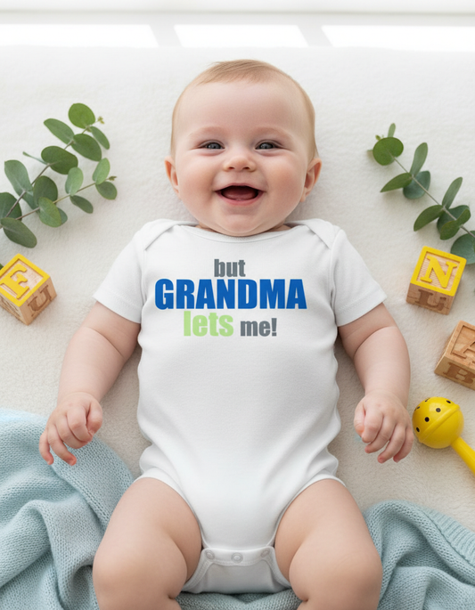 Happy baby wearing But Grandma Lets Me white onesie with blue and green lettering, sitting with colorful props including yellow blocks and blue blanket