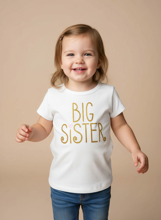 Toddler wearing white Big Sister t-shirt with gold letters in professional studio setting