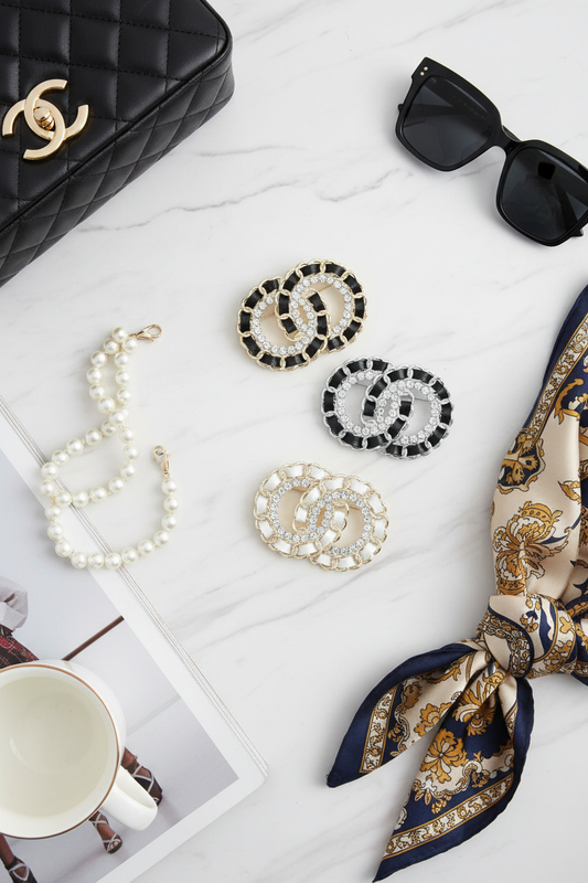 Crystal CC brooches styled with designer handbag, silk scarf, and luxury accessories on marble surface