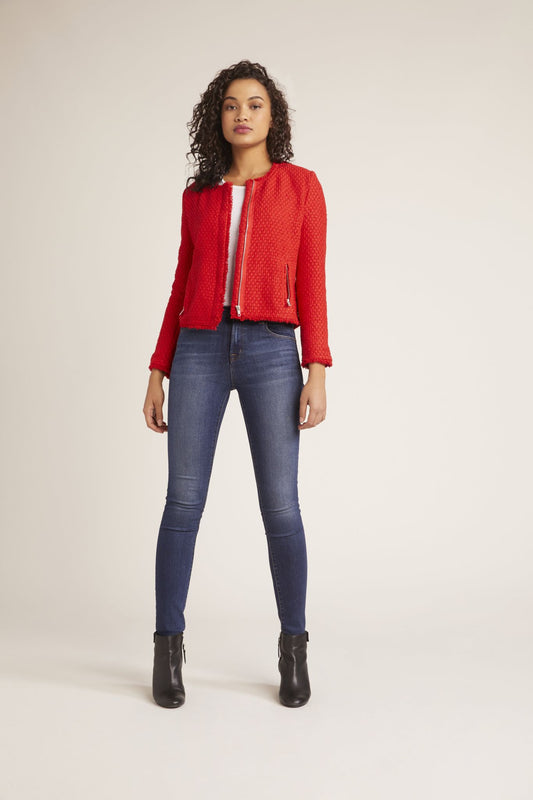 Woman wearing a red jacket, blue jeans, and black boots on a white background