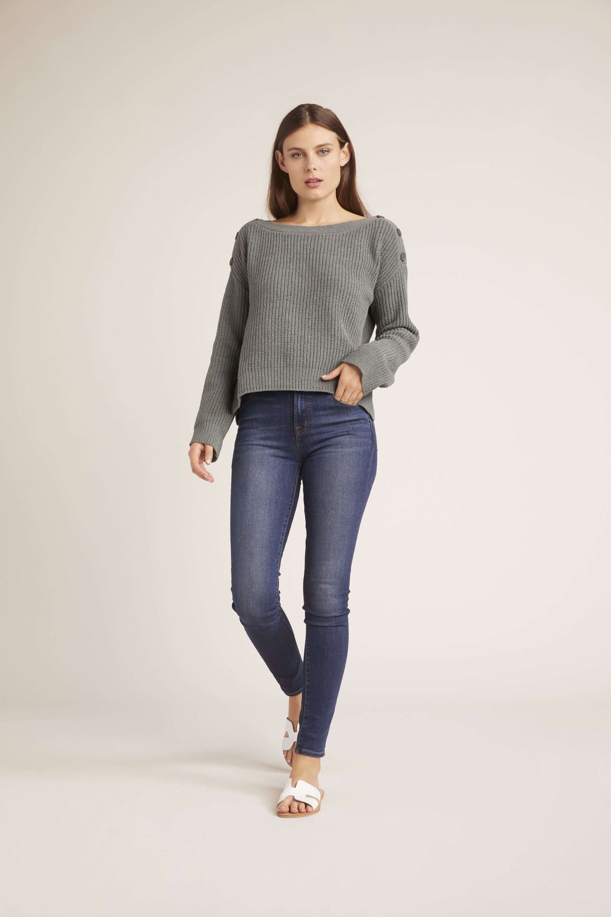 Woman wearing an olive sweater and blue jeans on a plain background