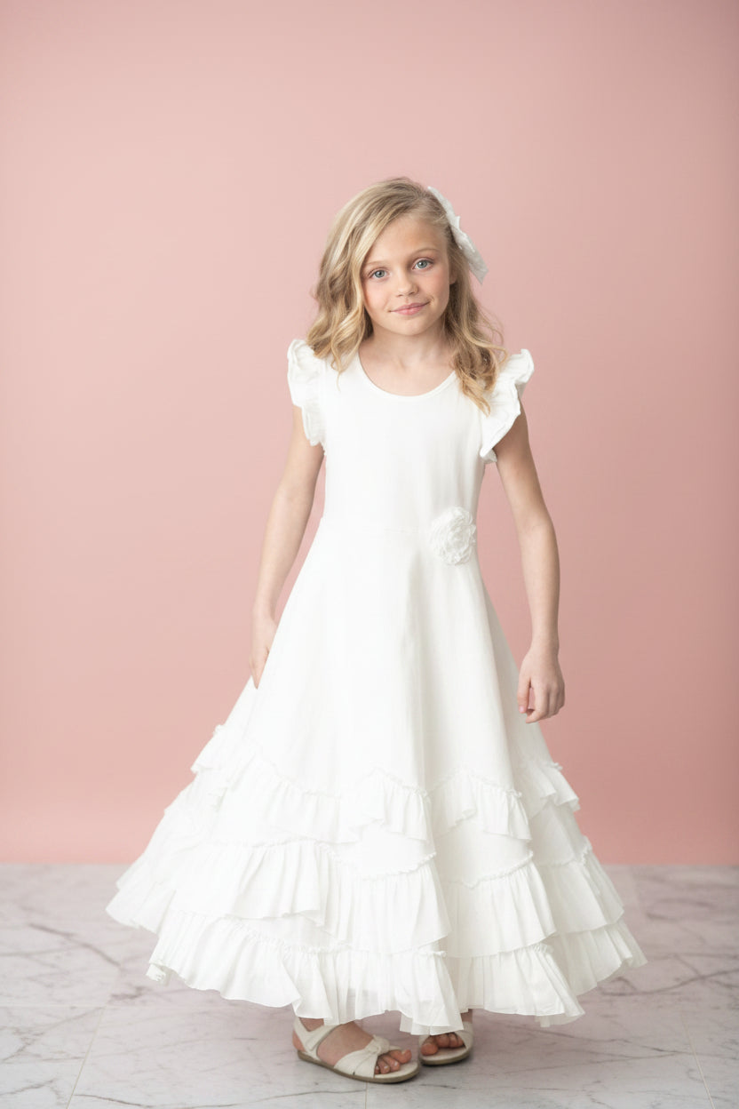 Young girl wearing ivory white ruffle maxi dress with tiered ruffles and rosette details for flower girl or formal occasion