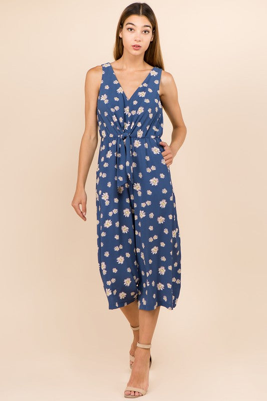 A model wearing a blue floral gaucho jumpsuit with a V-neckline and sleeveless design.