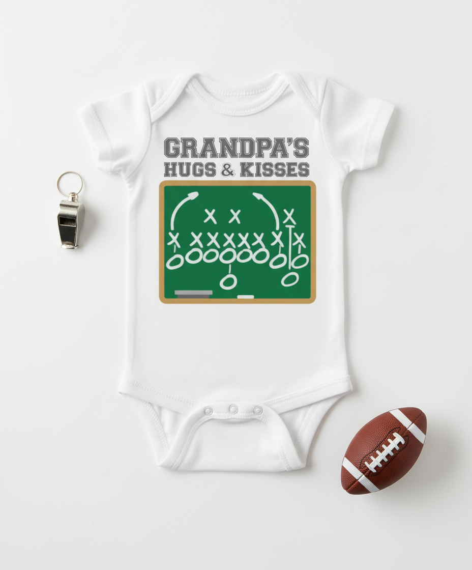 Flat lay of white Grandpa's Hugs & Kisses onesie with football play diagram and sports props on white background