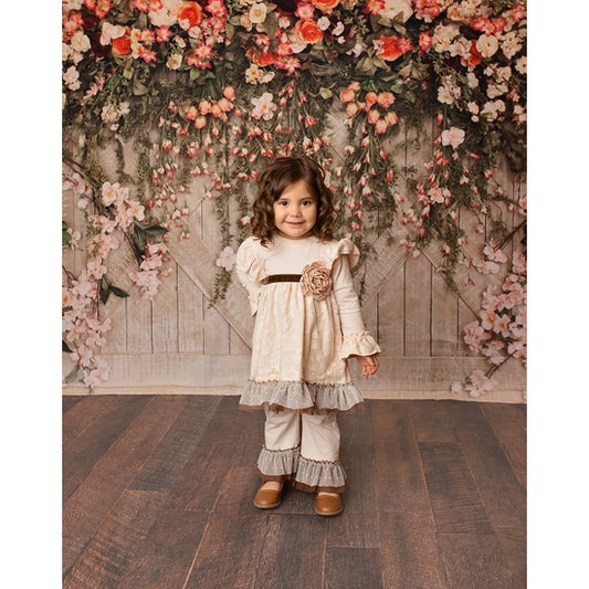 Young girl wearing cream swing top with brown velvet ribbon and gray tulle ruffle pants in floral setting