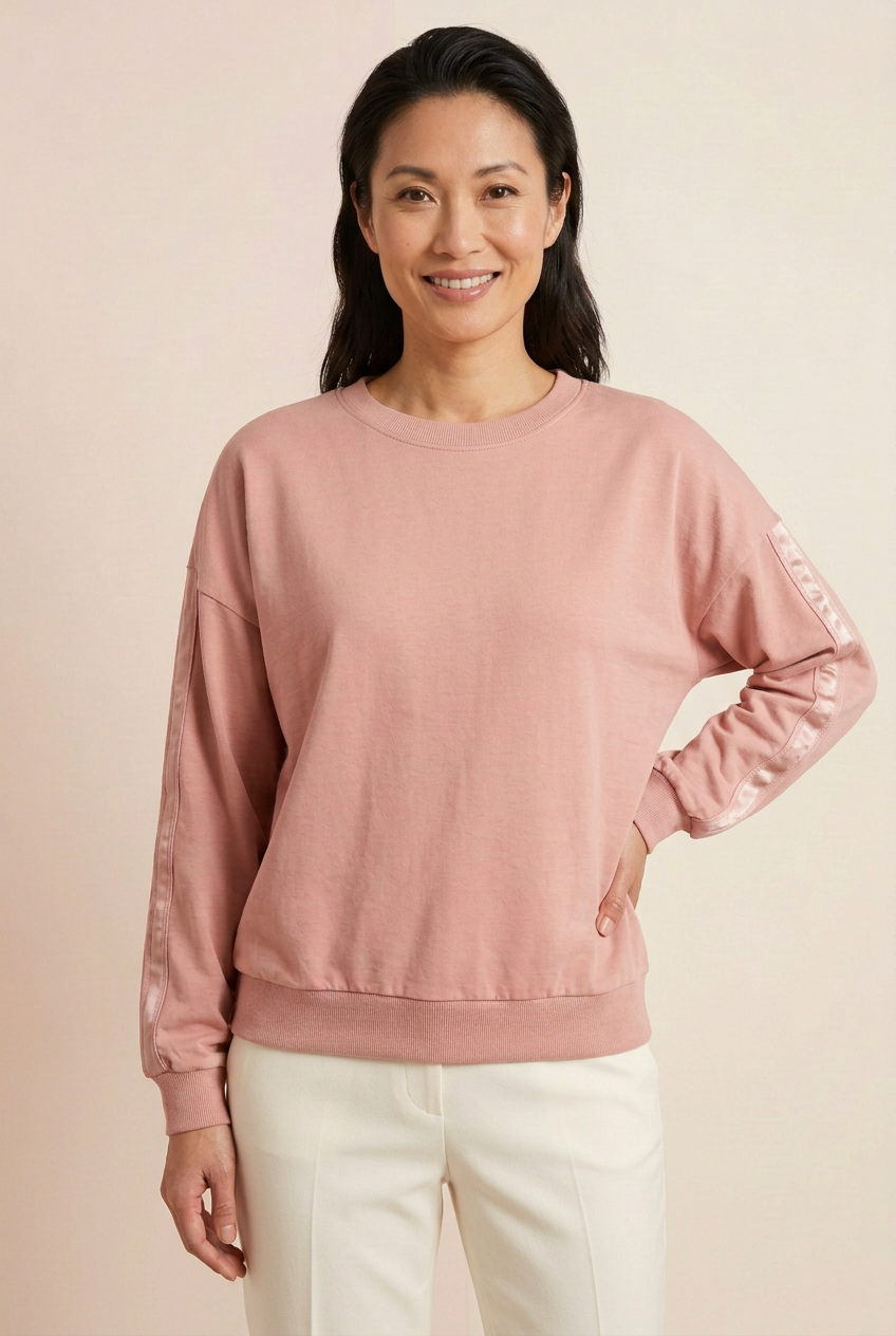 Blush drop-shoulder pullover with rippled satin sleeve trim and ivory trousers, three-quarter hand-on-hip view