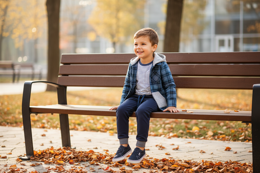Young boy wearing blue plaid hooded flannel jacket over striped tee with navy joggers playing outdoors in autumn park setting