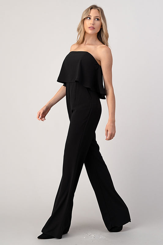 Woman wearing black strapless wide-leg jumpsuit with ruffle detail, side view showing silhouette and movement