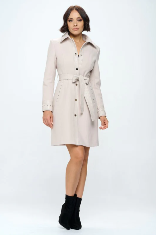 Model wearing blush pink belted faux wool dress coat with button-front closure and stud details over white top and light wash jeans