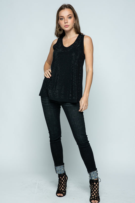 A woman wearing a sleeveless black top with rhinestones, paired with black jeans and black heels.
