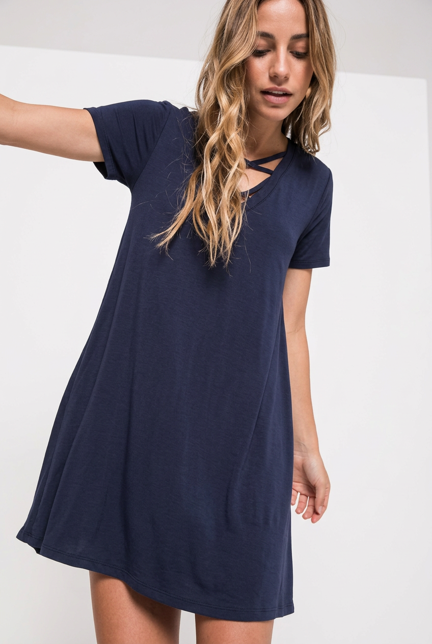 Navy double-crisscross V-neck T-shirt swing dress on a long-haired blonde model in an arm-extended front pose against a pale studio backdrop.