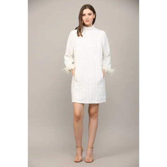 Woman wearing white textured mini dress with feather-trimmed sleeves and mock neck, full-length front view
