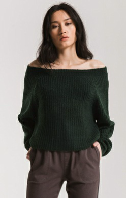 Woman wearing a dark green off-shoulder sweater against a plain background
