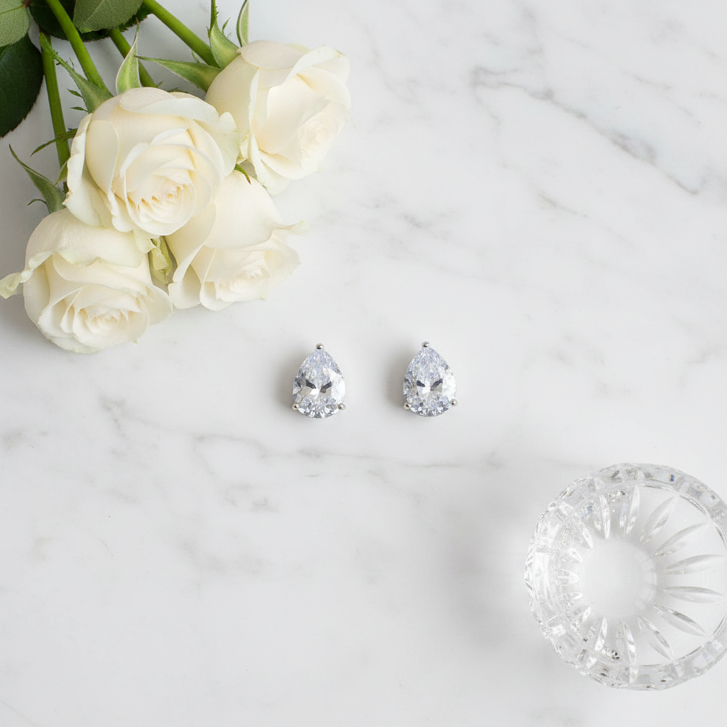 Petite teardrop cubic zirconia stud earrings in silver styled with white roses and crystal dish on marble surface