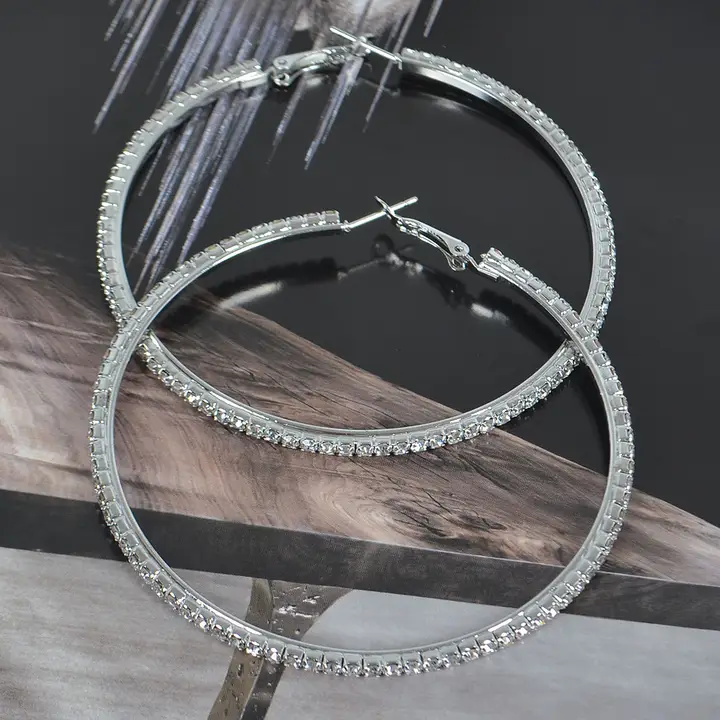 Silver rhinestone hoop earrings on driftwood branch, featuring sparkling clear crystal embellishments along entire 3-inch hoop with detailed view of hinge clasp mechanism