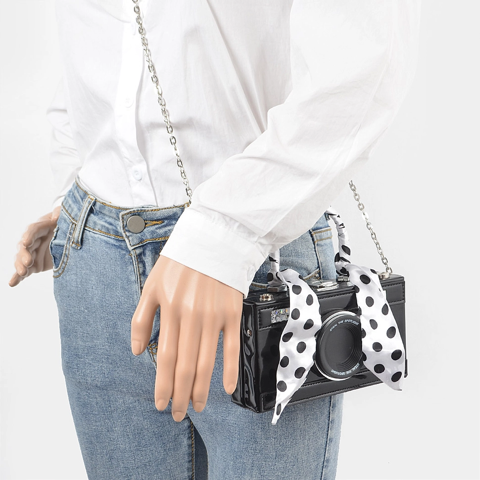 Woman wearing black metallic mirror camera clutch with polka dot scarf crossbody style with jeans and white shirt