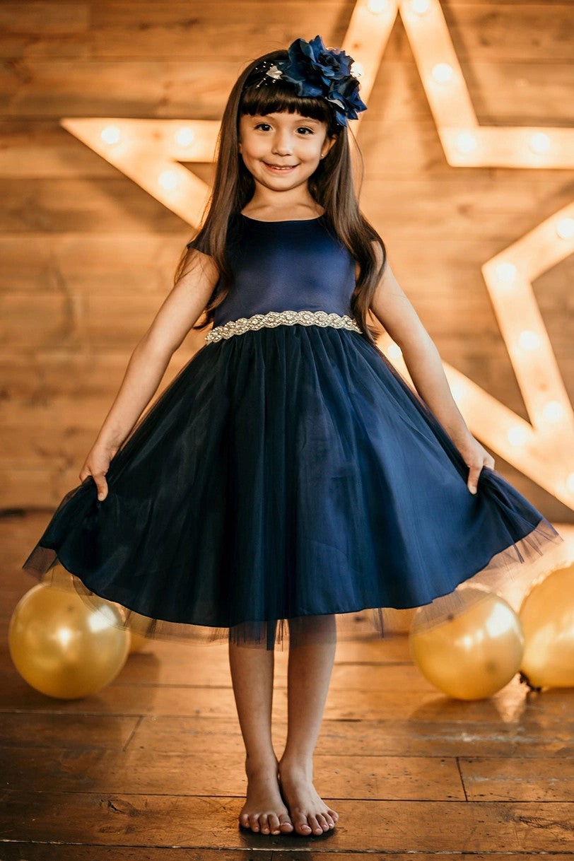Young girl wearing navy blue satin dress with rhinestone waist belt at party with gold balloons