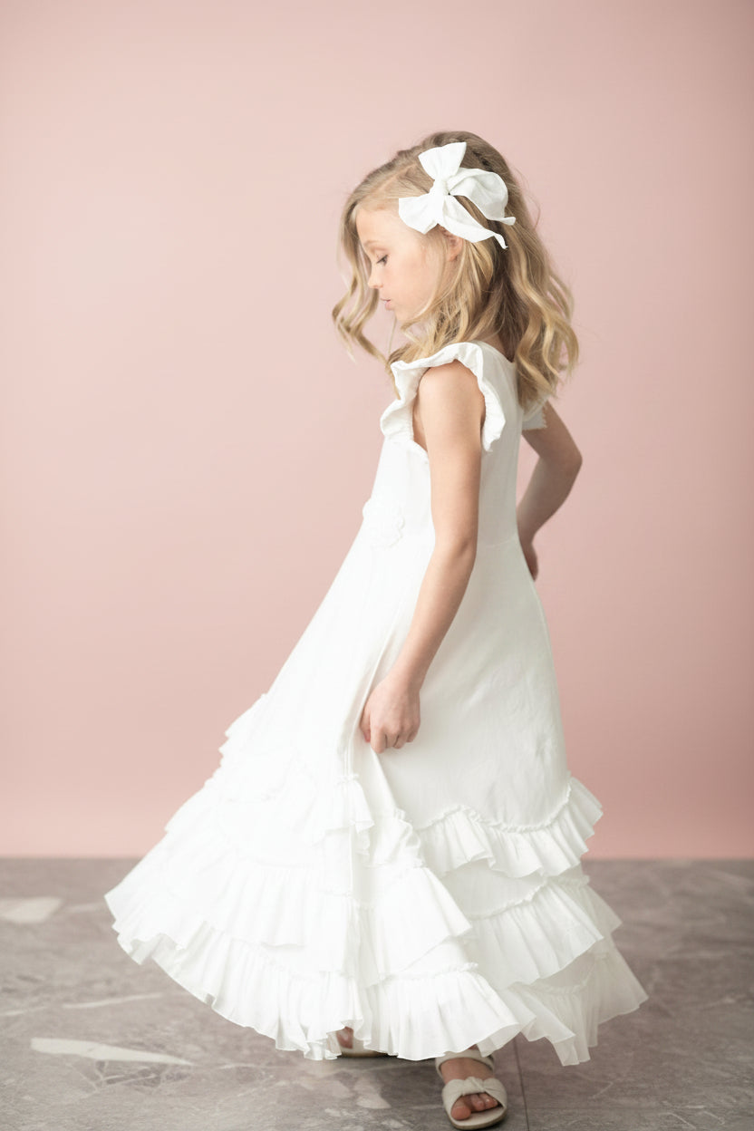 Side view of girls ivory maxi dress showing flutter sleeves and cascading tiered ruffle layers with rosette accents