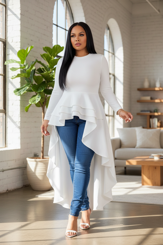 Plus size woman in white hi-low ruffle long sleeve top styled with skinny jeans and heeled sandals — women's fashion editorial