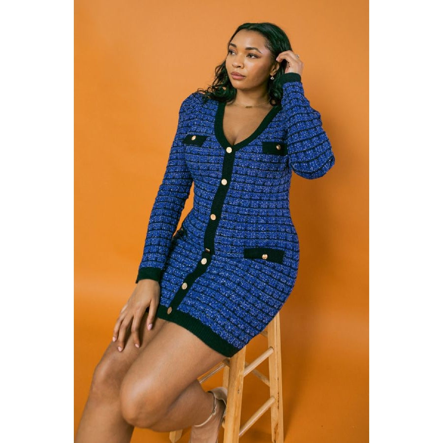 Woman wearing royal blue tweed mini dress with black contrast trim and gold button details, seated against orange background