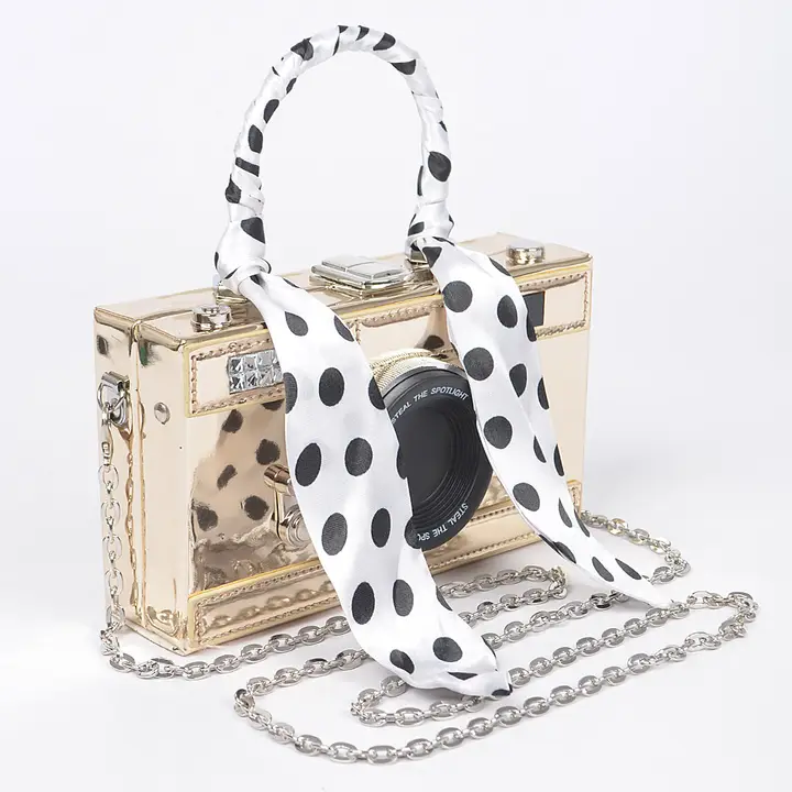Gold metallic mirror camera clutch with polka dot scarf on handle and silver chain strap on white background