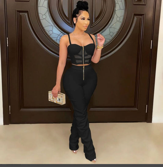 A woman wearing a black ruched 2-piece pant set with a sleeveless top and matching pants, standing in front of a wooden door.