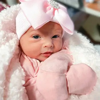Baby girl wearing pink newborn hat with sparkly bow and matching pink outfit