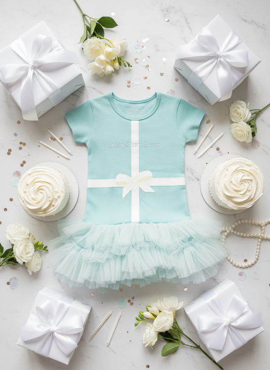 Tiffany blue toddler tulle dress with white ribbon bow surrounded by birthday celebration elements including gift boxes, candles, confetti, and white flowers on marble background