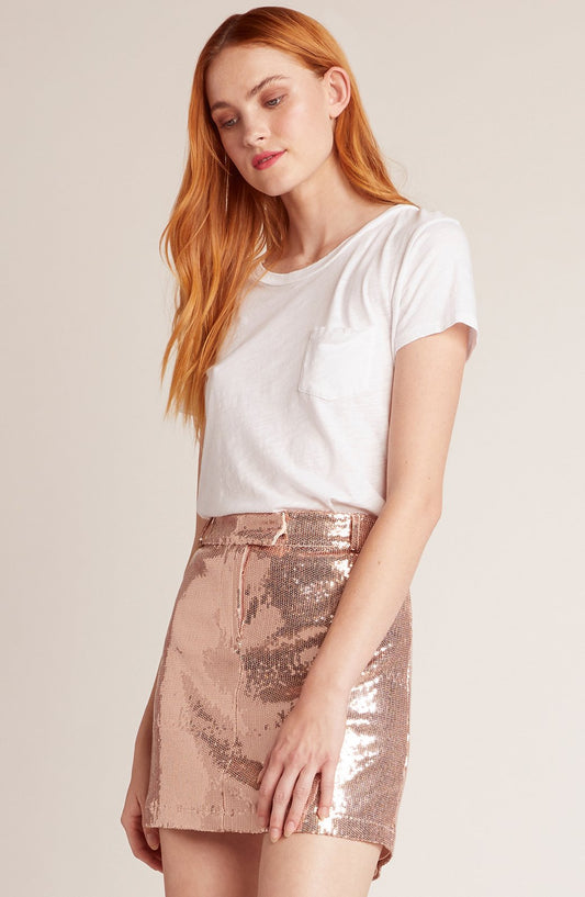 Woman wearing a white t-shirt and rose gold sequin skirt on a plain background