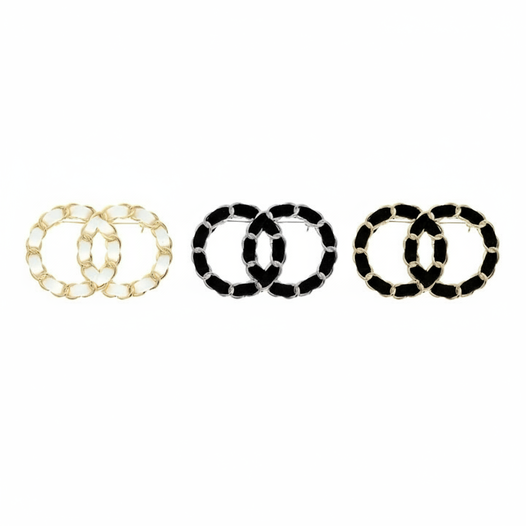 Three interlocking double O logo brooches displayed in row showing color variations - gold with white enamel, silver with black enamel, and gold with black enamel on white background