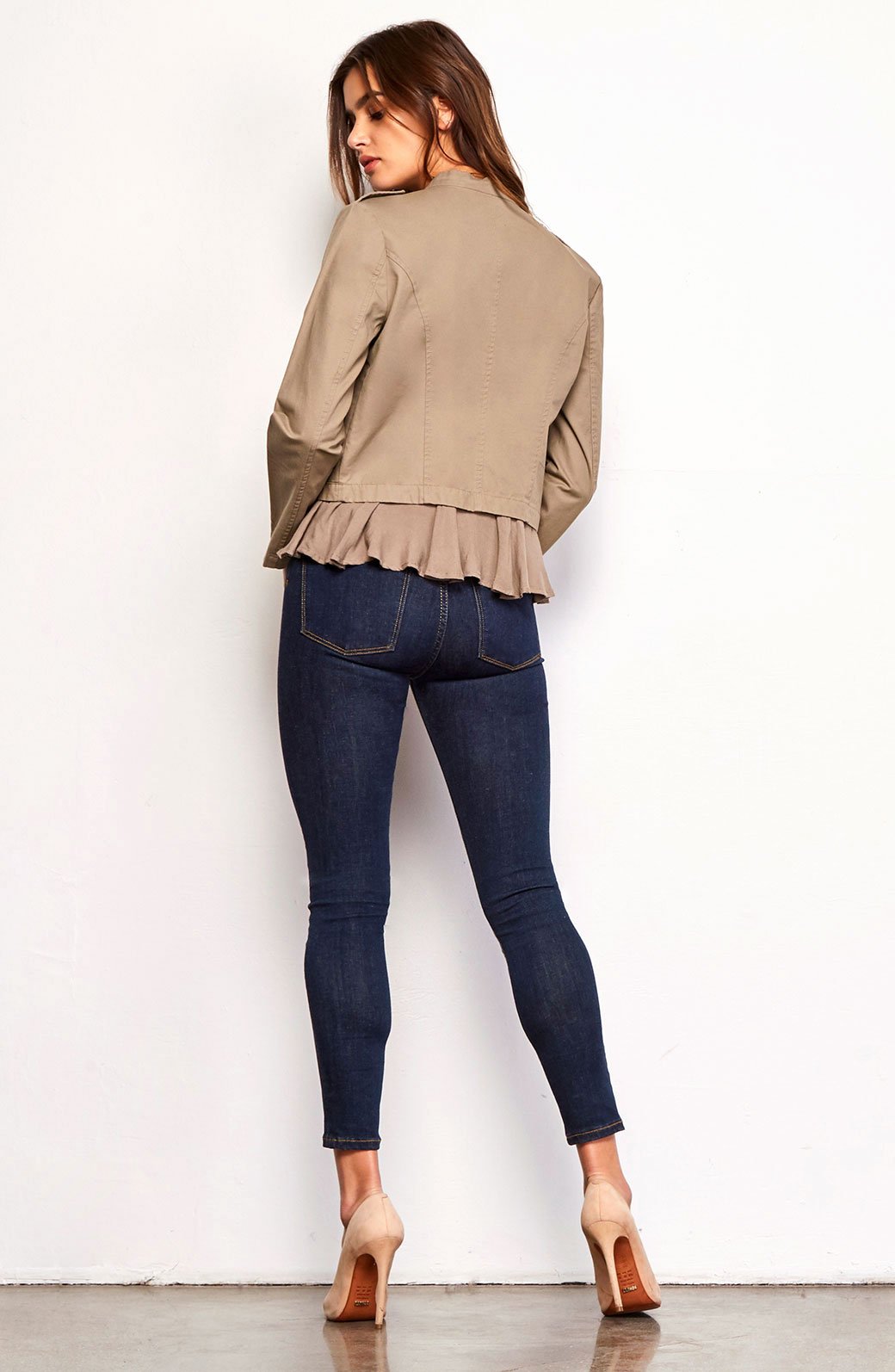 Woman wearing a beige jacket and dark blue jeans against a white background