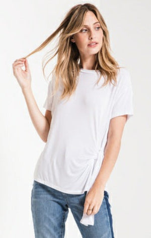 A woman modeling a white short-sleeve t-shirt with a side twist detail, paired with blue jeans, against a plain white background.
