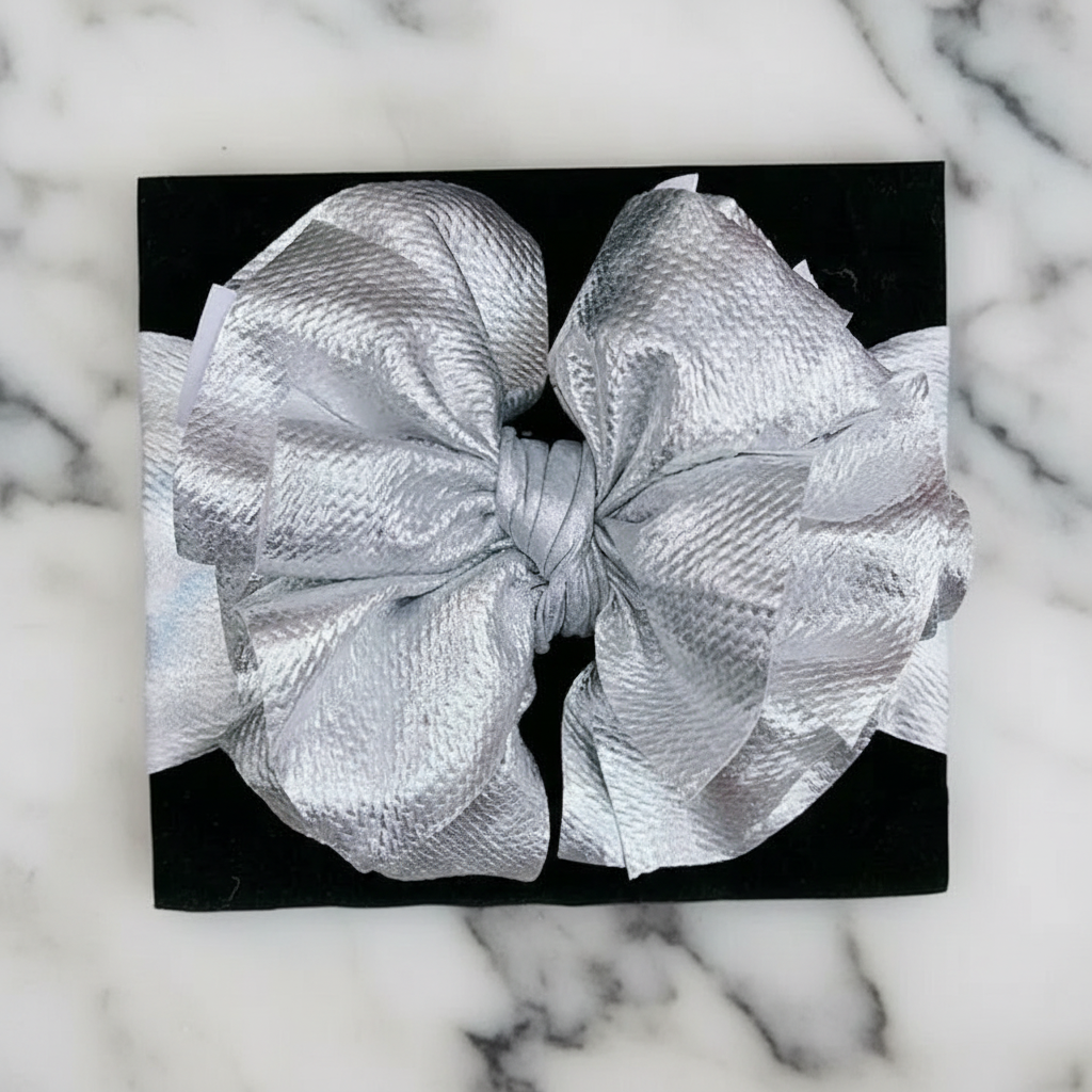Metallic silver statement bow headband on black background showing full 7-inch bow width
