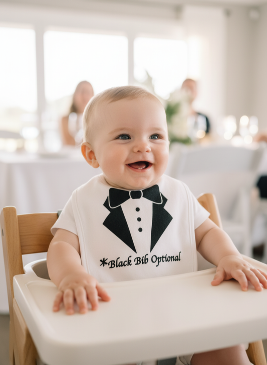 Happy baby wearing white Black Bib Optional tuxedo bib with black bow tie design at baby shower celebration with pastel decorations and balloons