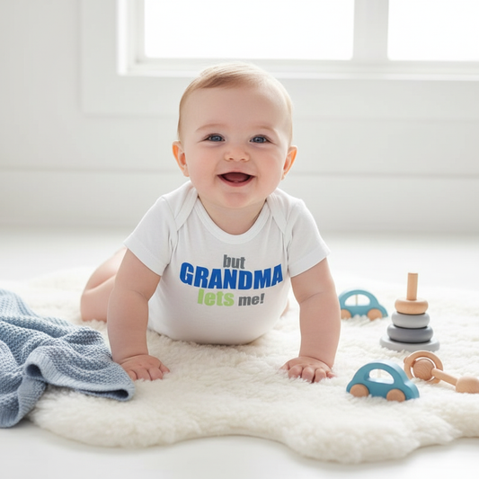 Baby boy wearing white "But Grandma Lets Me!" onesie while sitting and playing with colorful toys
