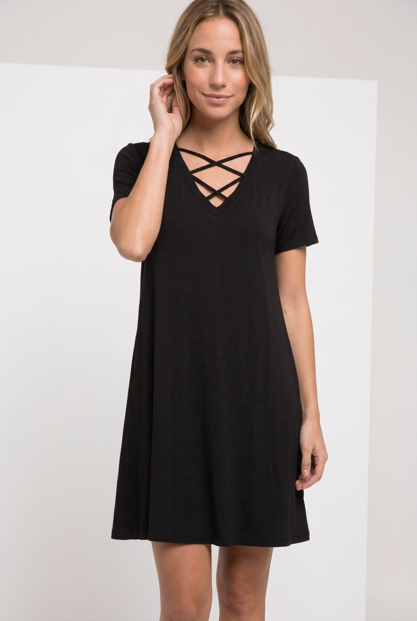 Black double-crisscross V-neck T-shirt swing dress in lightweight jersey, shown on a blonde model in a relaxed hair-tuck pose.