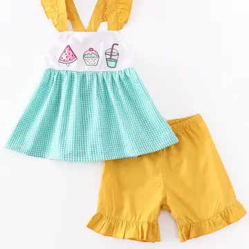 Children's outfit with a white top, green checkered skirt, and yellow shorts on a white background