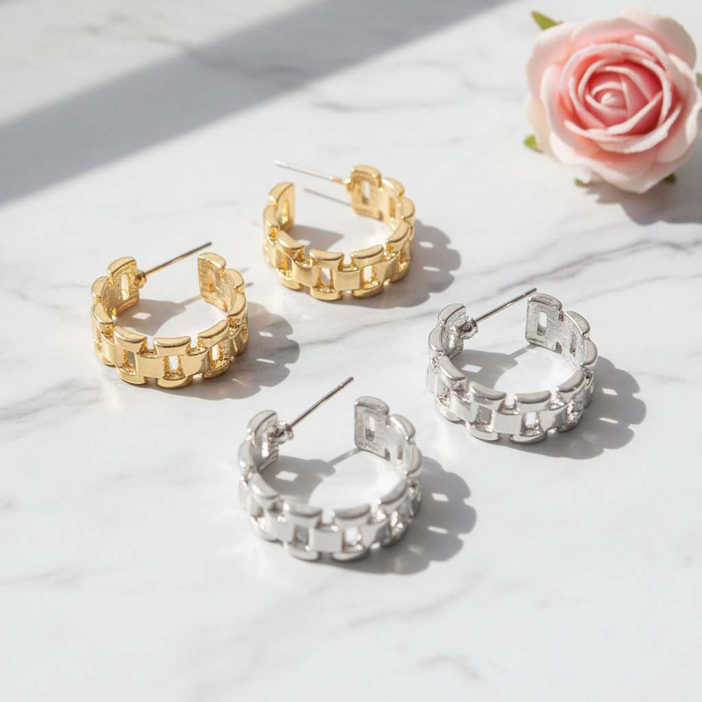 Gold and silver chain link hoop earrings displayed on white marble surface with pink rose as subtle accent prop, earrings as main focus, luxury jewelry photography
