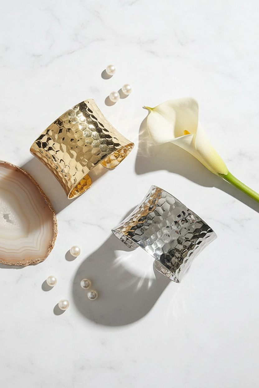 Wide hammered cuff bracelets in gold and silver on marble with refined modern styling



