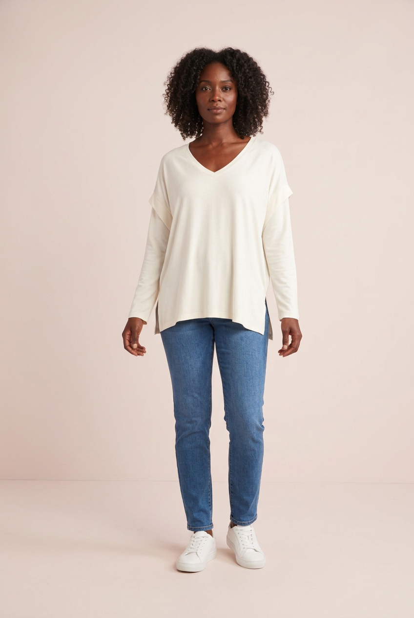 Ivory relaxed V-neck long sleeve top styled with blue jeans and white sneakers for casual weekend outfits, front model view on a pink backdrop.